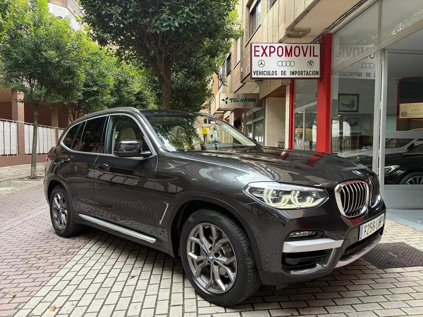 Un BMW X3 está estacionado frente a un concesionario de automóviles.