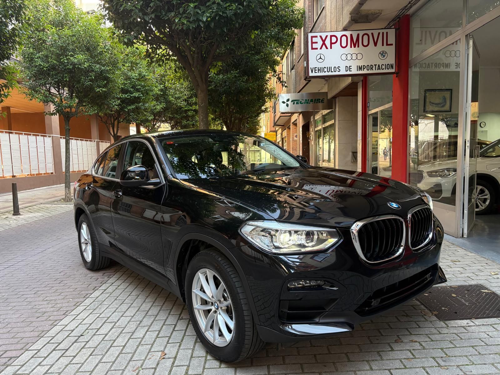 Un BMW X4 negro está estacionado frente a un concesionario de automóviles.