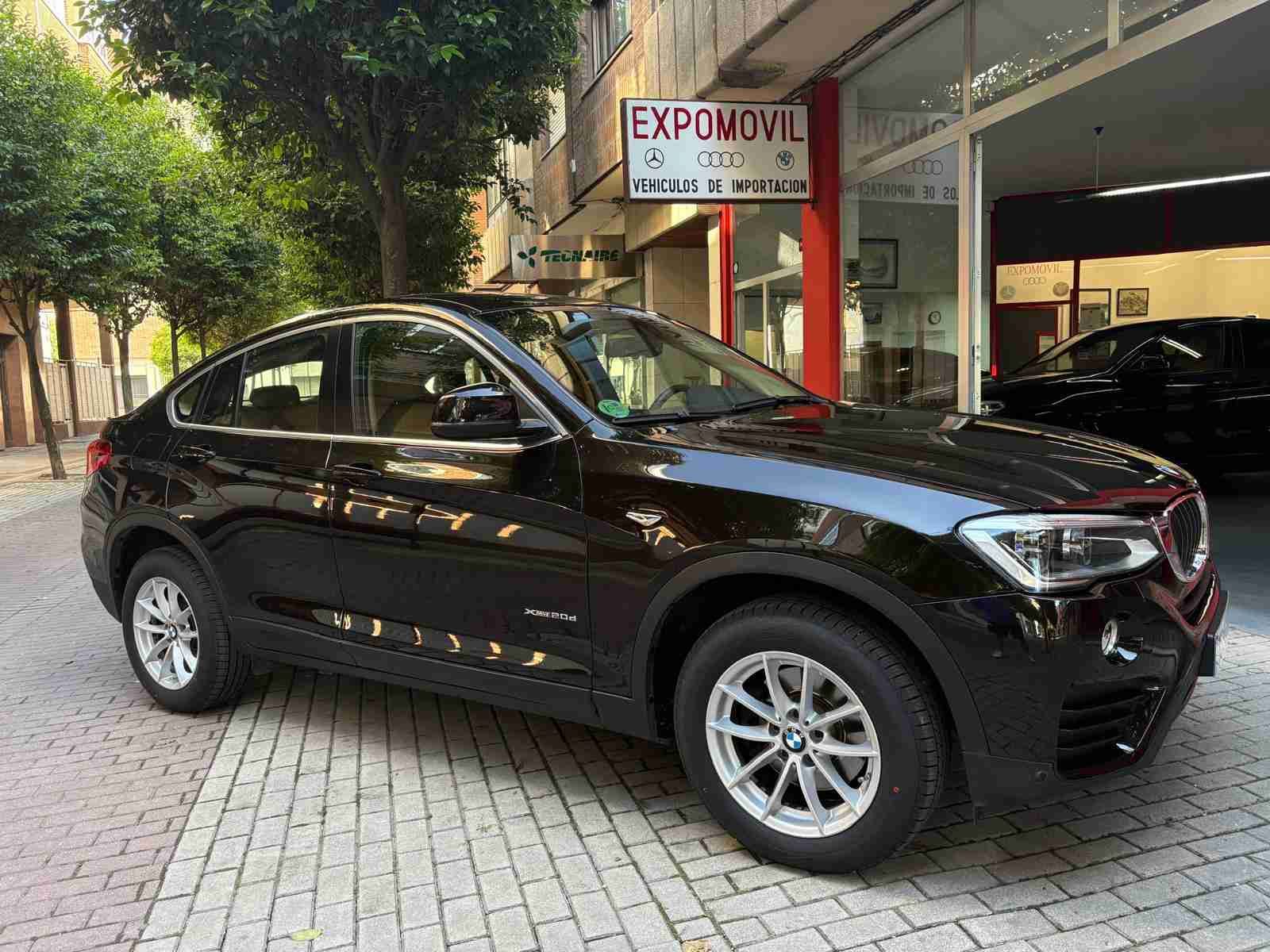 Un BMW X4 negro está estacionado frente a un concesionario de automóviles.
