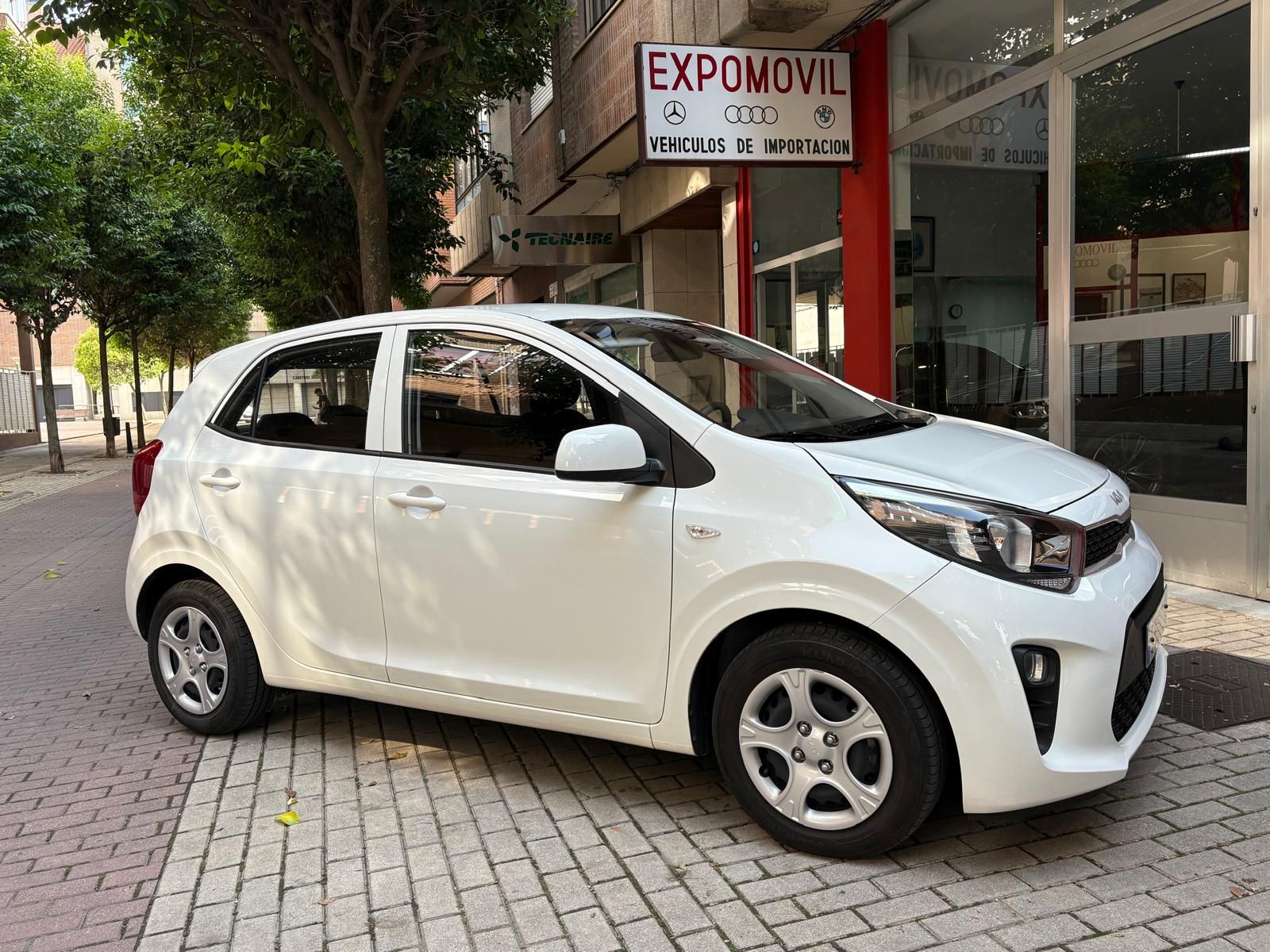 Un coche blanco está aparcado delante de un concesionario de automóviles.