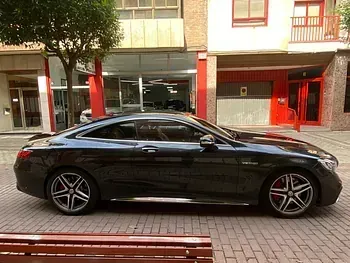 Un coche deportivo negro está estacionado en una acera de ladrillos frente a un edificio.