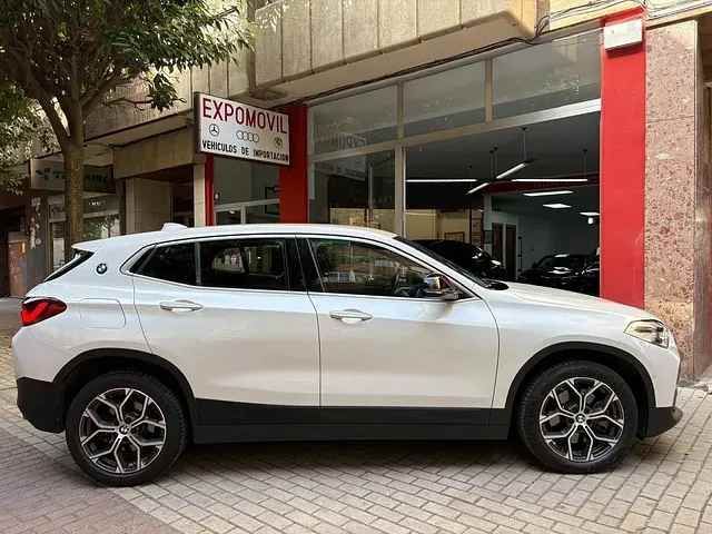 Un BMW X2 blanco está estacionado frente a un concesionario de automóviles.