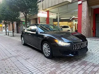 Un Maserati Ghibli negro está estacionado en una acera de ladrillos frente a un edificio.