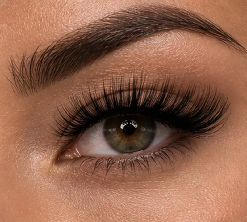 Primer plano de un ojo marrón con pestañas largas y maquillaje de cejas bien definido.