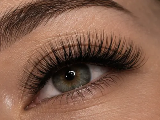 Primer plano de un ojo marrón con pestañas largas y maquillaje de cejas bien definido.
