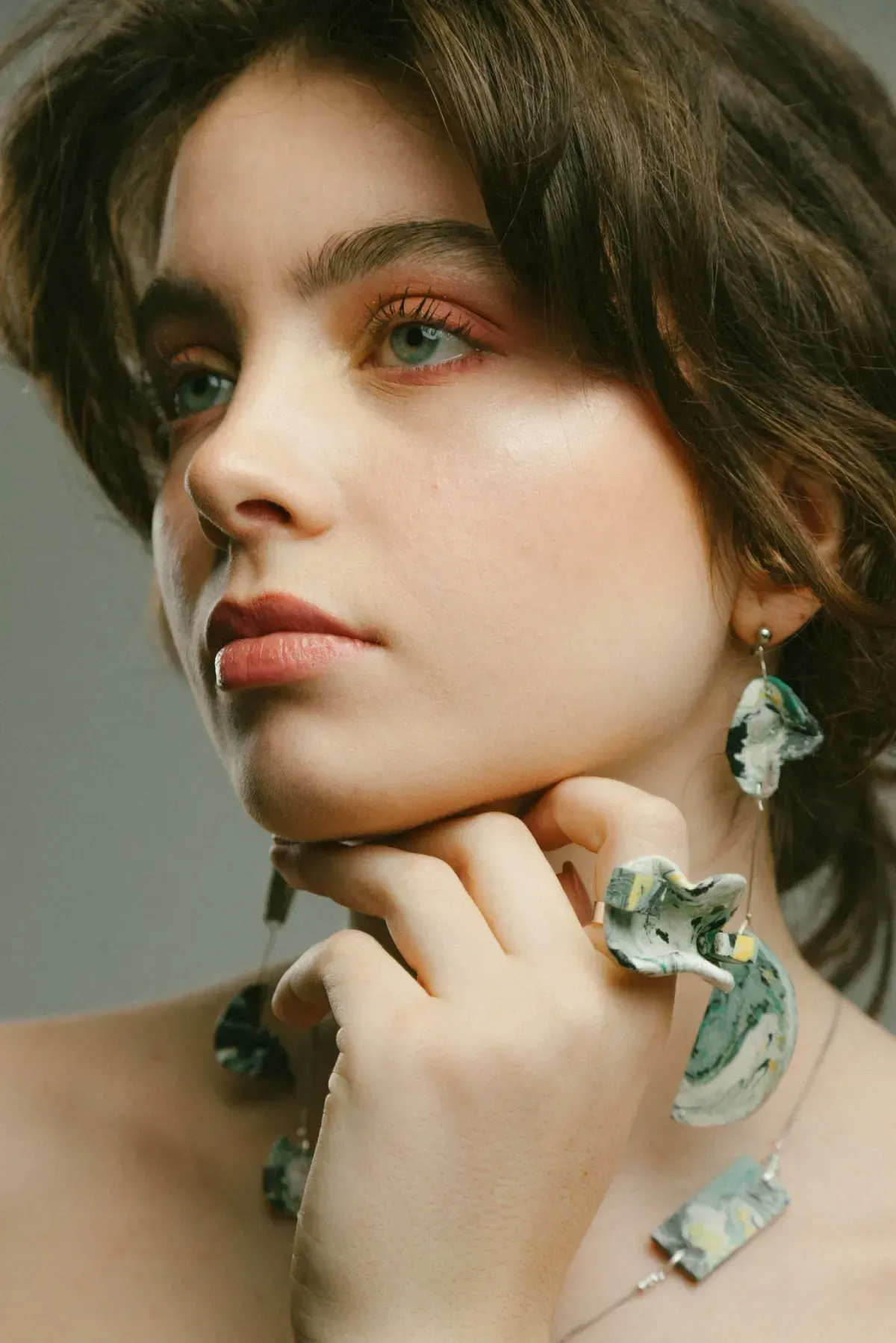 Retrato de una persona con cabello castaño corto, joyas de turquesa y expresión pensativa sobre un fondo neutro.