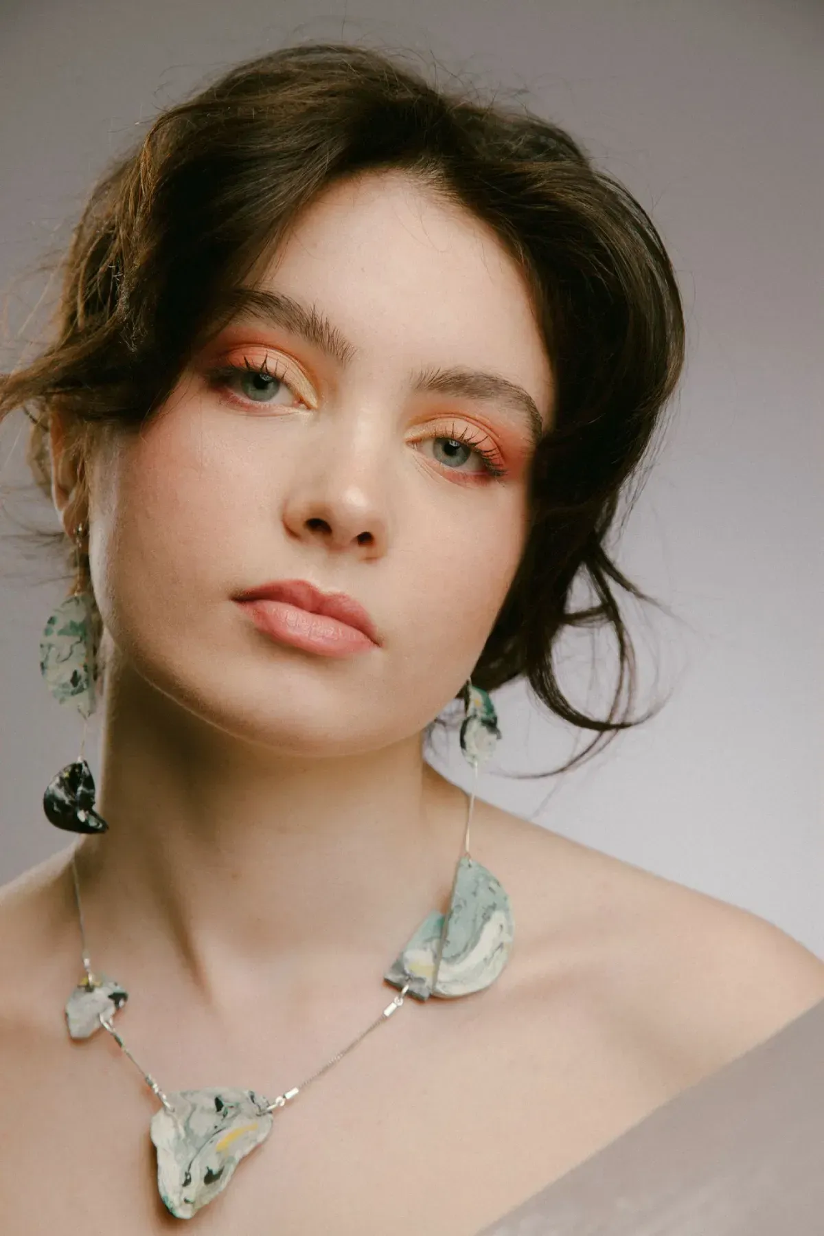 Retrato de estudio de una persona con cabello oscuro que lleva un collar floral pálido y maquillaje suave.