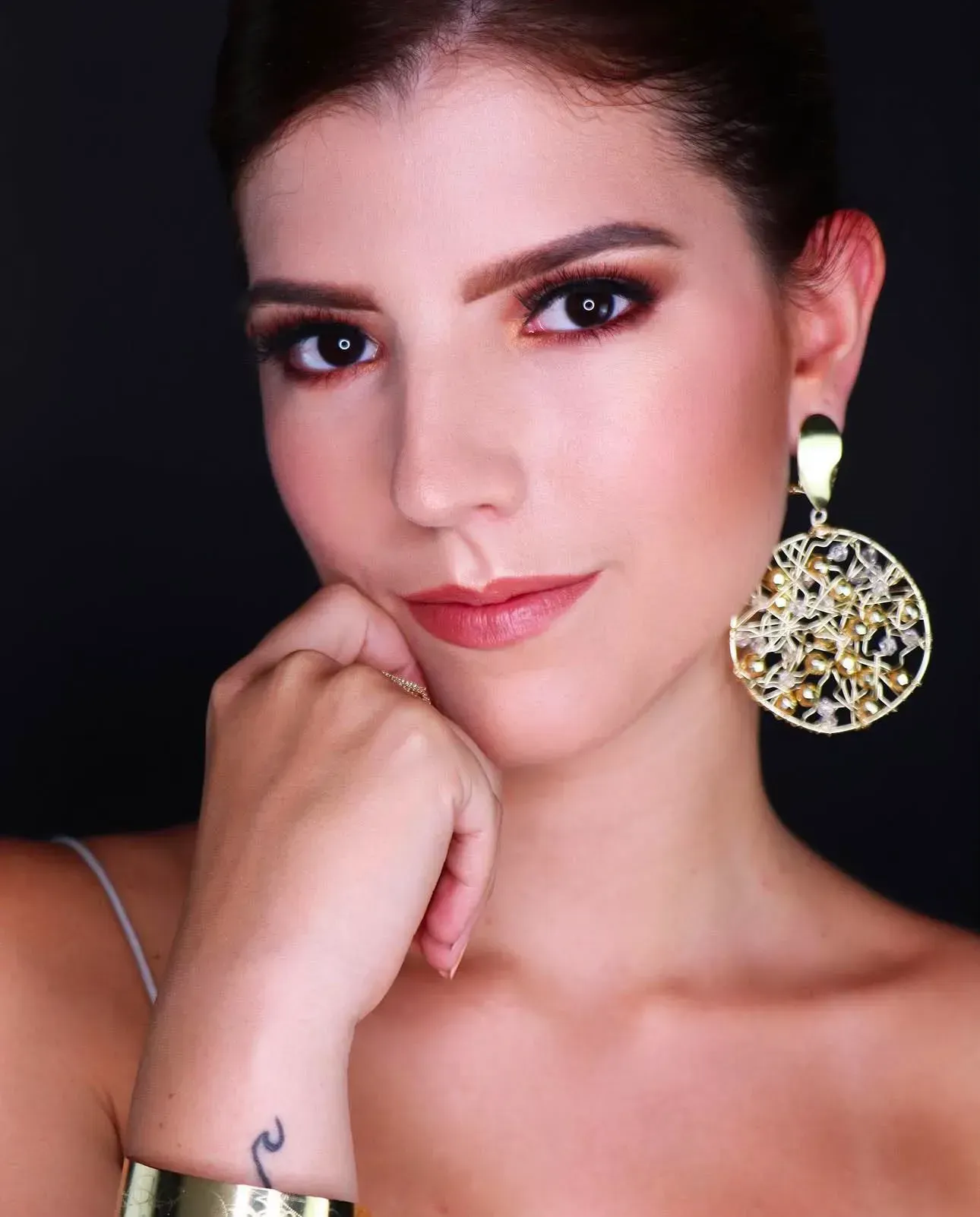 Retrato de una mujer de cabello oscuro, con la barbilla apoyada en la mano, luciendo un gran pendiente de oro.