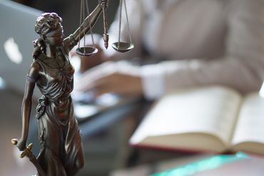 Eine Statue der Justitia steht auf einem Tisch neben einem Buch.