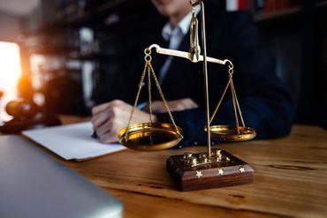 Ein Richter sitzt an einem Schreibtisch und vor ihm liegt eine Waage der Gerechtigkeit.