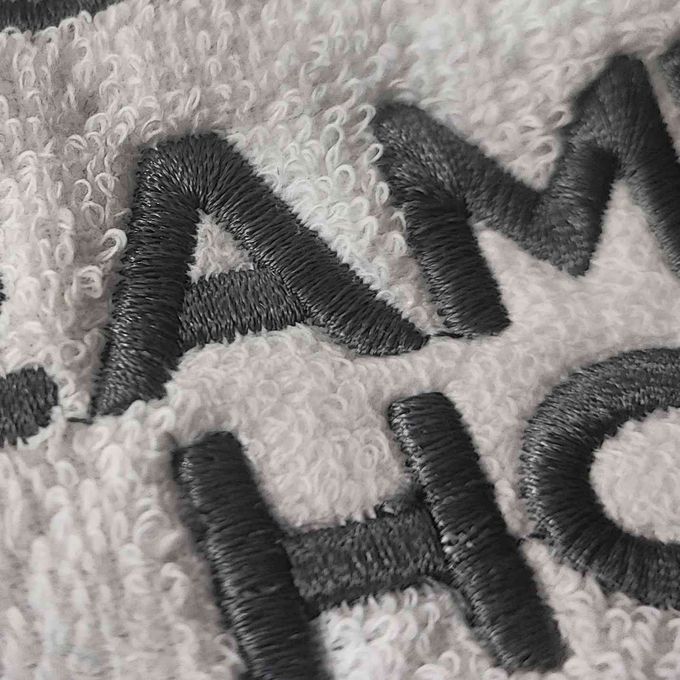 Primer plano de letras negras bordadas sobre una toalla de tela texturizada de color blanco roto.