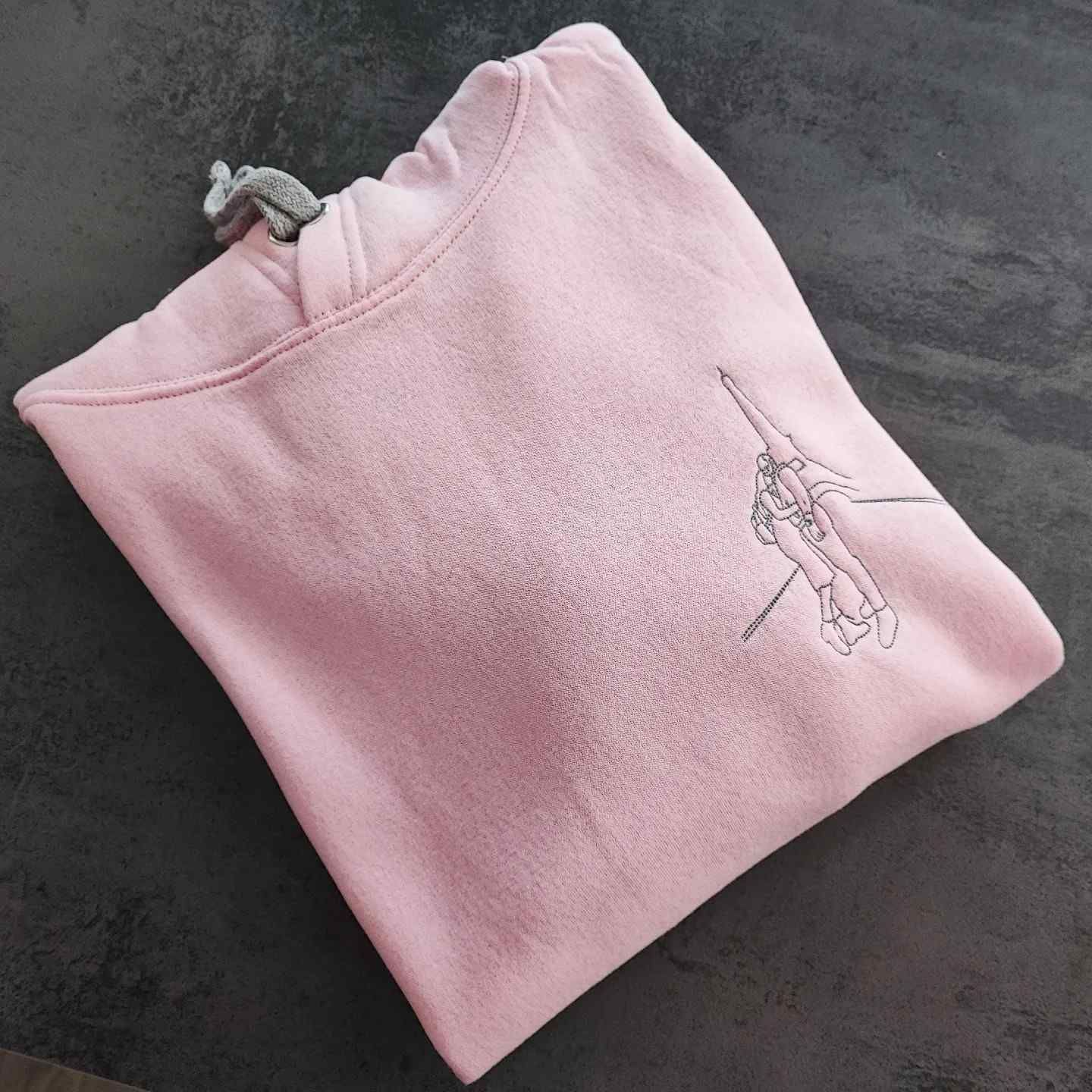 Una sudadera con capucha de color rosa claro, con cordón gris y un delicado dibujo lineal negro de una persona.