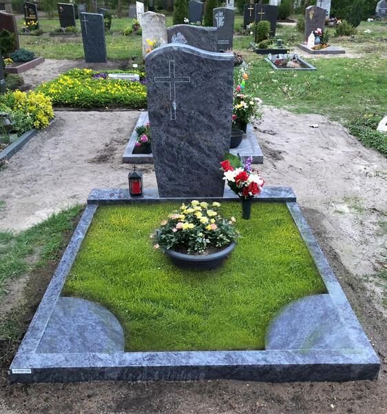 Grabstein auf einem Friedhof mit einem ordentlich gepflegten grünen Grabbett, Blumen und Kerzen.