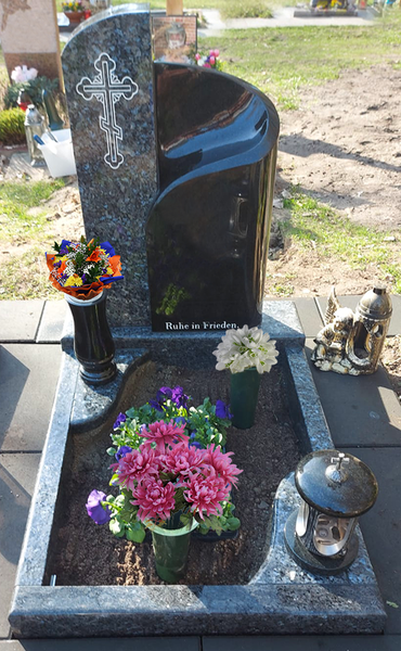 Grabstätte aus schwarzem Granit mit Blumen, Kerzen und einem Gedenkkreuz.