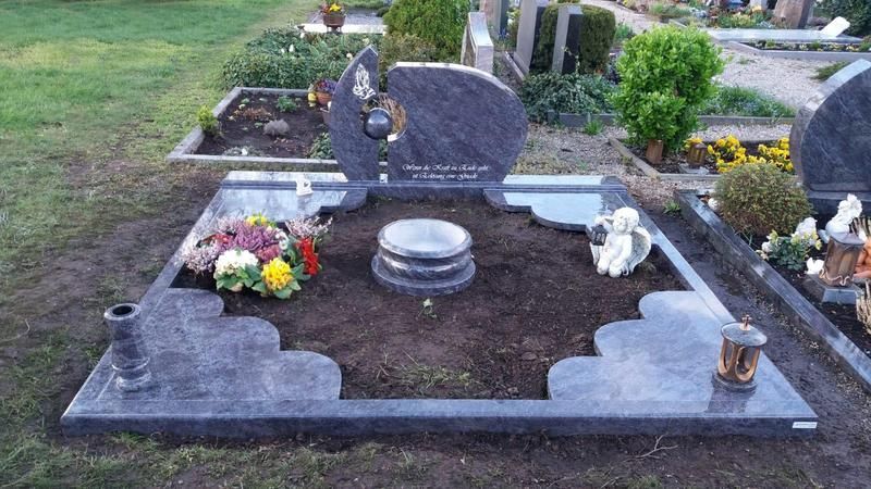 Grabstelle auf dem Friedhof mit grauem Grabstein, Blumenstrauß und dunklem Erdrand