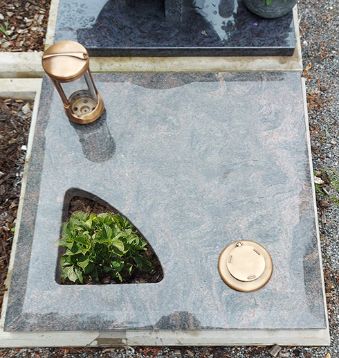 Grabstein mit Messinglaterne und rundem Vasenhalter auf einer Granit-Gedenkplatte, mit einer kleinen bepflanzten Aussparung.