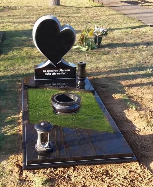 Schwarzer, herzförmiger Grabstein auf einem polierten schwarzen Grab mit grünen Rasenakzenten auf einem Friedhof.