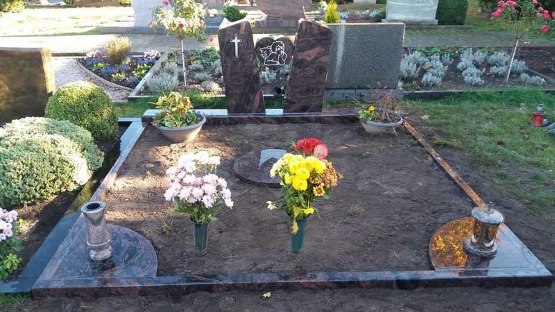 Grab mit Blumen und Kerzen auf einem Friedhof, mit zwei dunklen Grabsteinen und einem gepflegten Gedenkplatz