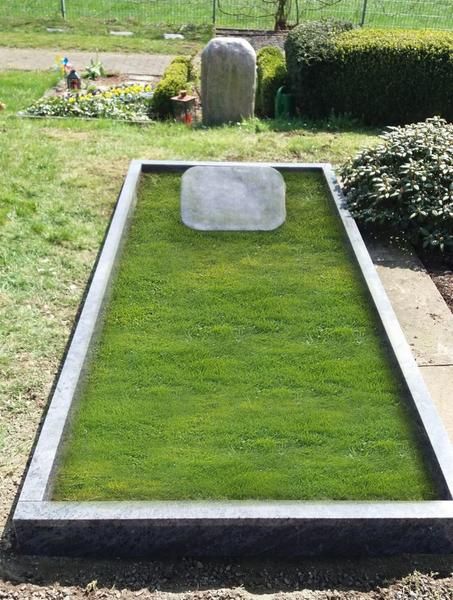 Rechteckige, grasbewachsene Grabstätte mit grauem Grabstein auf einem Friedhof, eingefasst von einer Betonumrandung.