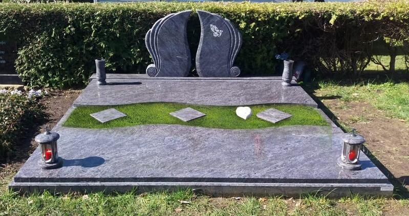 Gedenkgrabstein aus Granit mit Blumenschmuck auf einem grasbewachsenen Friedhofsplatz