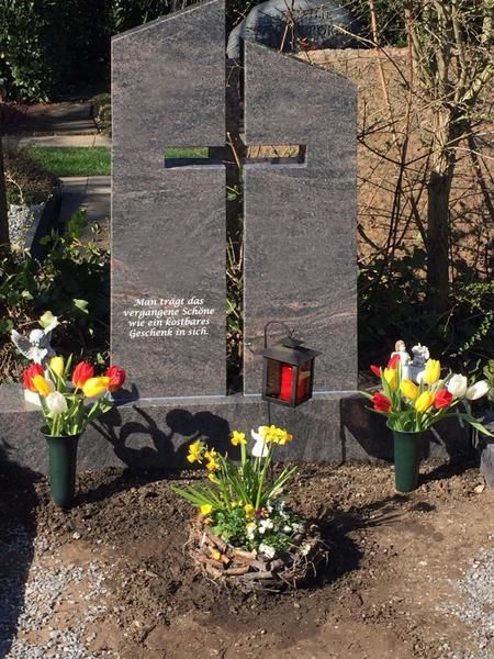 Gedenkkreuz aus Granit mit Blumen und Kerzen an einer Grabstätte im Freien