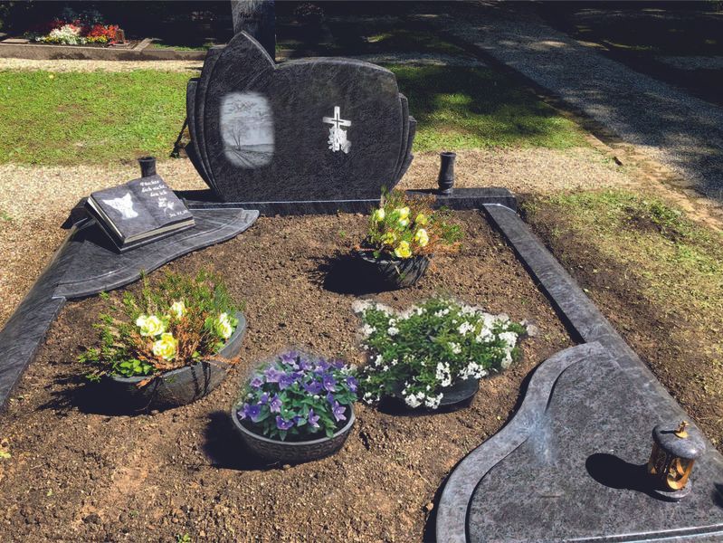 Gedenkgarten mit Kies, schwarzem Grabstein und mehreren bunten Blumentöpfen