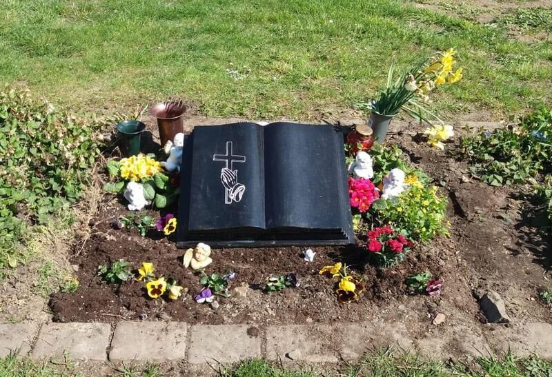 Grab mit einem offenen schwarzen Gedenkbuch und Blumen auf einem grasbewachsenen Friedhofsplatz