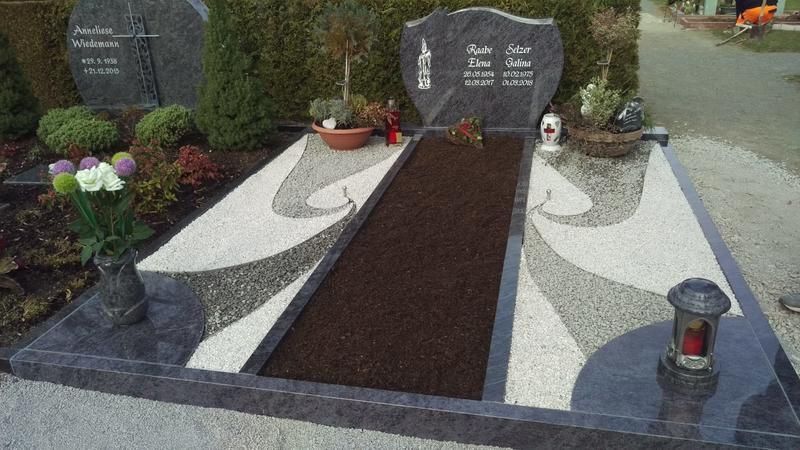 Friedhofsgrab mit dunklem Grabstein, weißem Kies, braunem Mittelstreifen, Blumen und Kerzen