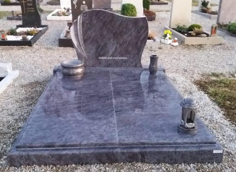 Poliertes Grabdenkmal aus schwarzem Granit auf einem Friedhof mit Blumenvasen und einem Grabstein im Hintergrund