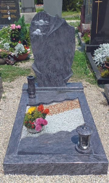 Grab aus grauem Granit mit Blumen und zwei Kerzen in einem Friedhofsgarten