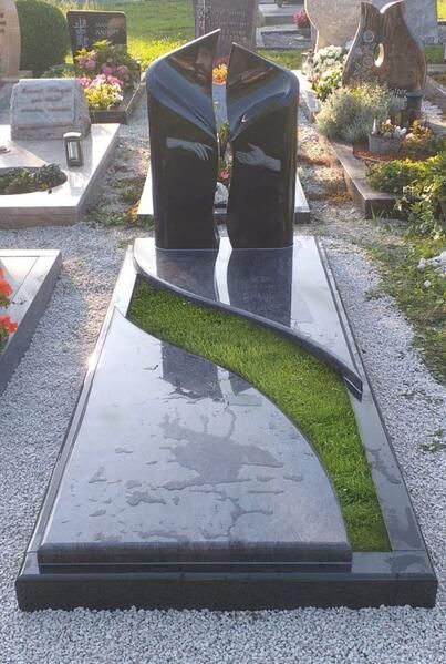 Modernes Denkmal aus schwarzem Granit mit grüner, S-förmiger Einlage auf einem Friedhof
