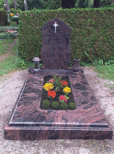 Marmorgrab mit weißem Kreuz und bunten Blumen auf einem Friedhof.
