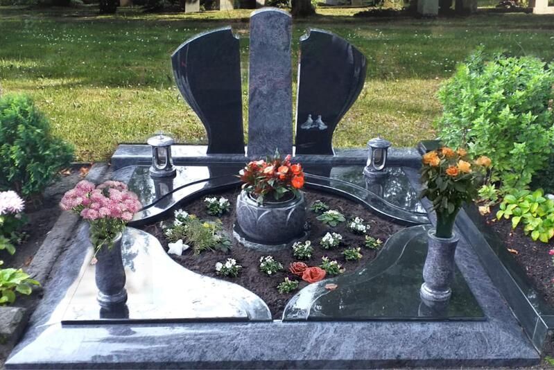 Ein mit Blumen und Kerzen geschmücktes Denkmal aus schwarzem Granit auf einem grasbewachsenen Friedhofsgelände
