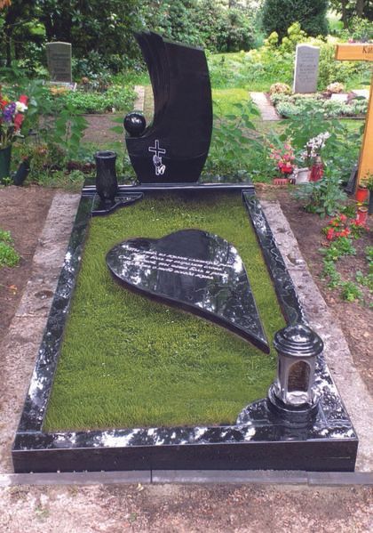 Schwarzer Granitgrabstein mit herzförmiger Gedenktafel in einem grünen Friedhofsfeld mit Blumen