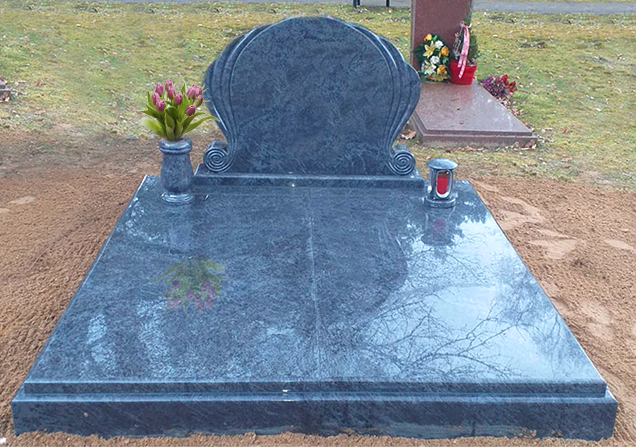 Schwarzer Granitgrabstein mit Blumenvasen und einer roten Kerze auf einem Friedhof