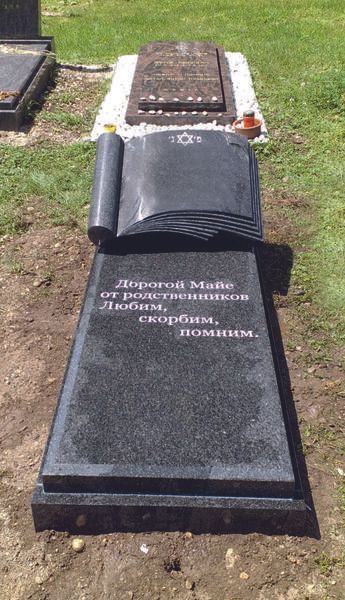 Gedenkgrabstein mit eingraviertem Namen, aus tiefschwarzem Stein, mit einem schwarzen Tuch bedeckt, auf einem grasbewachsenen Friedhofsplatz