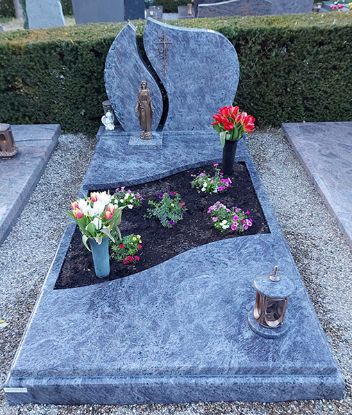 Granitgrabstein mit Blumen und Kerzen auf einem Friedhofsplatz