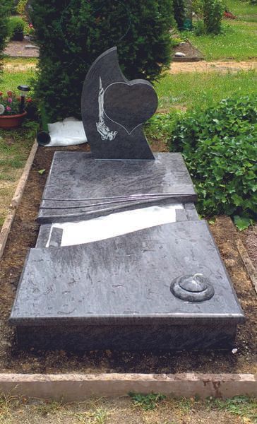 Schwarzer Granitgrabstein mit einem eingravierten Herz auf einem Friedhof, umgeben von Grün.