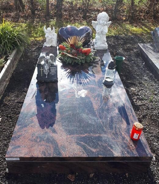 Marmorgrabstein mit Statuen, Blumen und Kerzen auf einem bewaldeten Friedhof.