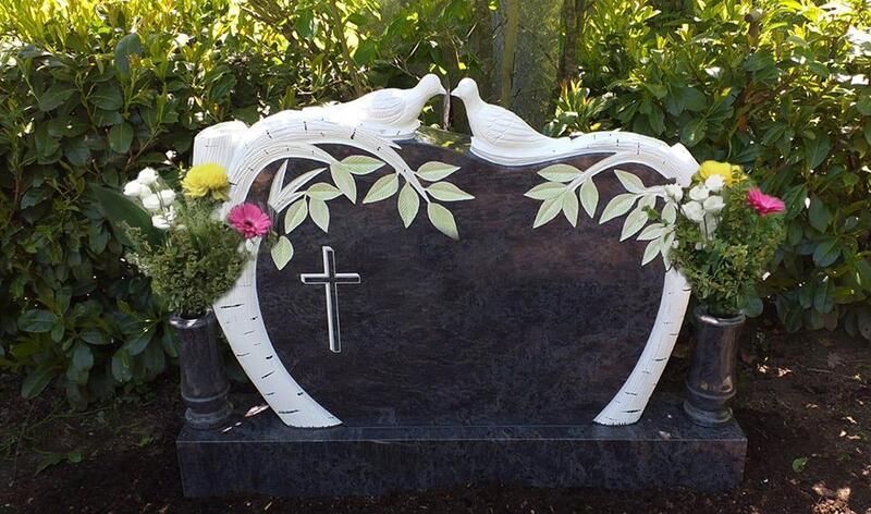 Schwarzer Grabstein mit weißen Tauben, Kreuz und floralen Verzierungen in einem Friedhofsgarten