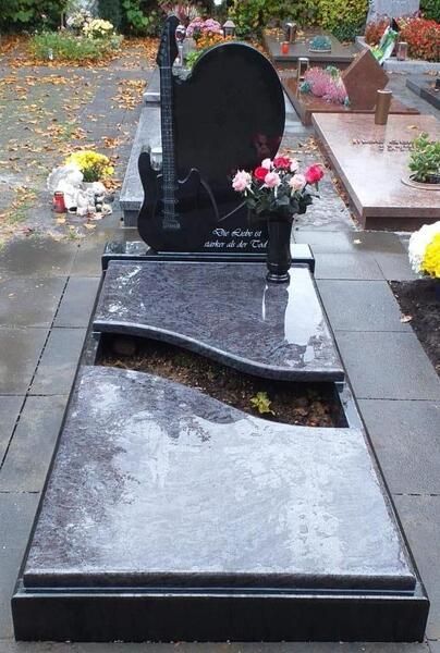 Schwarzer Granitgrabstein mit Blumen auf einem Friedhofsweg