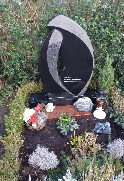 Moderner Granitgrabstein in einem Blumenbeet mit kleinen Gedenkornamenten.