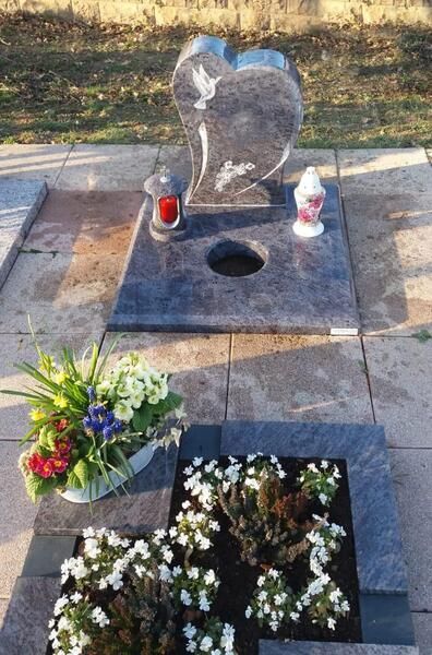 Grabstein mit herzförmigem Stein, Kerzen und Blumen auf einem Friedhofsplatz