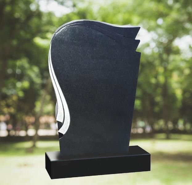 Schwarzes, aufrecht stehendes Granitdenkmal mit geschwungener weißer Einlage auf einem Sockel, im Freien vor verschwommenem Grün