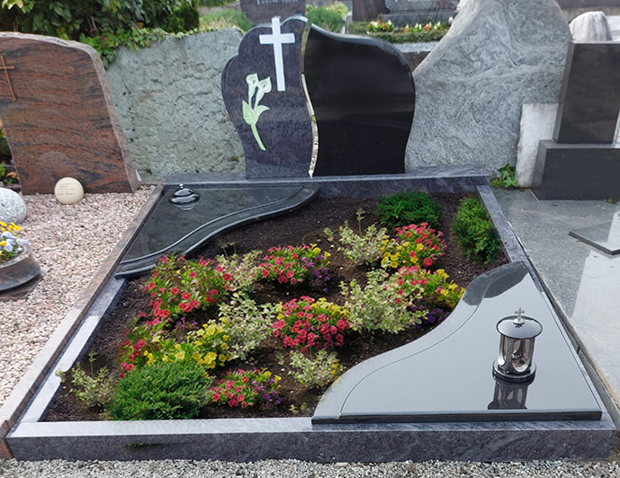 Schwarzes Granitgrab mit bunten Blumen und einer Laterne auf einem Friedhof