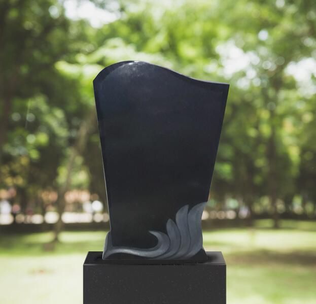 Schwarze abstrakte Skulptur auf einem Sockel in einer grünen Parklandschaft