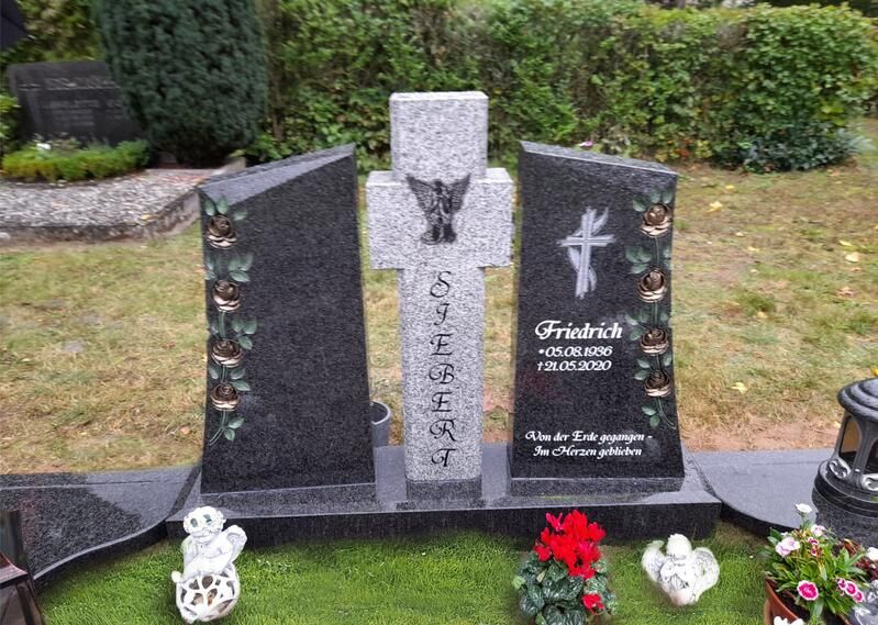Drei schwarz-graue Grabsteine ​​mit Blumen vor dem Hintergrund eines Friedhofsgartens