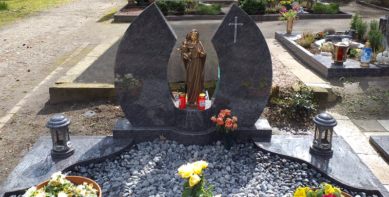 Grab mit dunklem Grabstein, Statue, Blumen und Kerzen auf einem Friedhof
