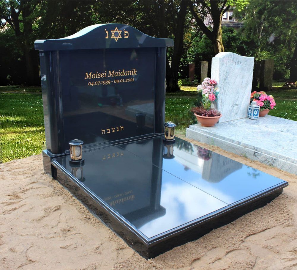 Schwarzer, polierter Gedenkgrabstein mit goldener Schrift und weißem Grabstein in einem Friedhofsgarten