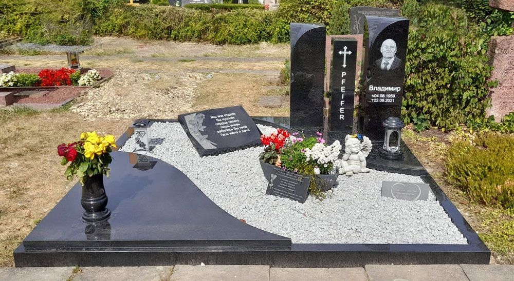Schwarzer und grauer Granitgrabstein mit Blumenvasen in einem Friedhofsgarten.